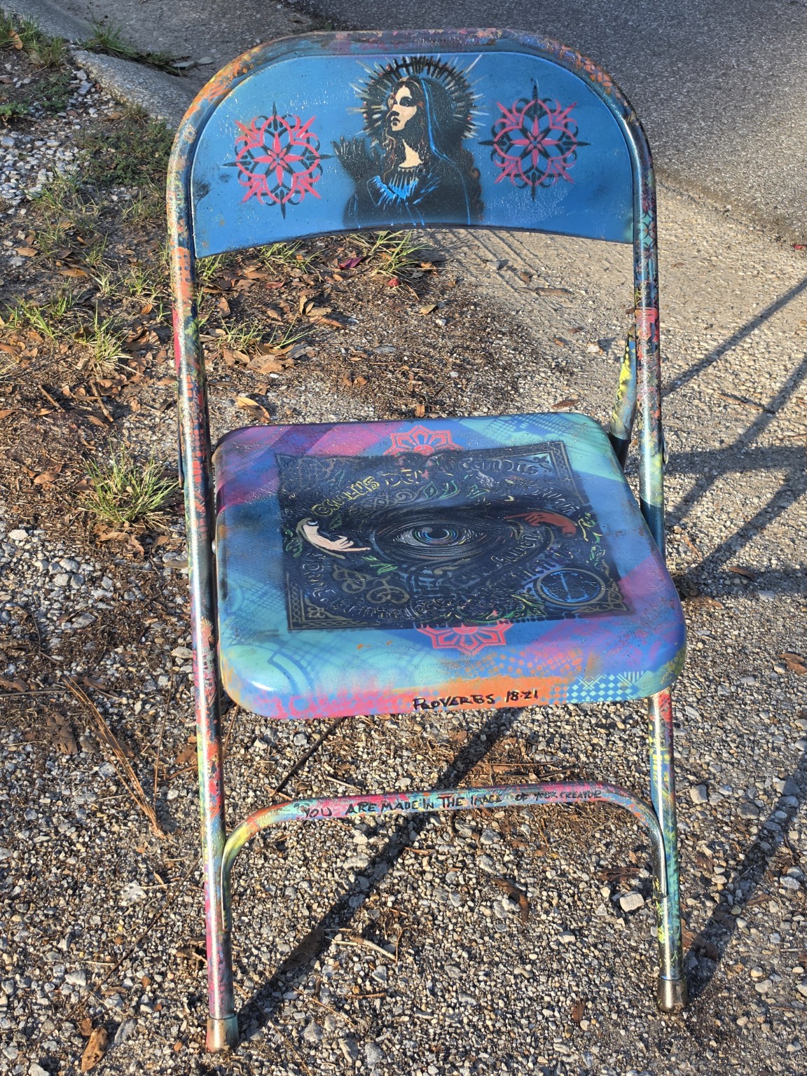 Front of a painted folding chair with a portrait on the backrest and a decorative eye on the seat